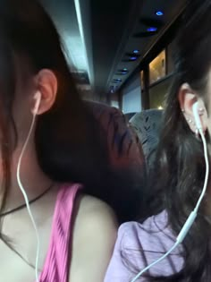 two young women sitting next to each other with ear buds in their ears and one woman looking at the camera