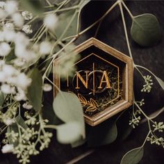 the logo for na is surrounded by greenery and white flowers on a black surface