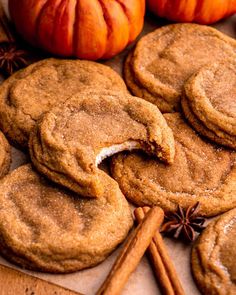 pumpkin spiced cookies are arranged on a table with cinnamon sticks and an orange pumpkin in the background