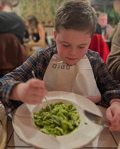 a young boy sitting at a table eating broccoli