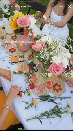 two women sitting at a table with flowers in vases on top of it,