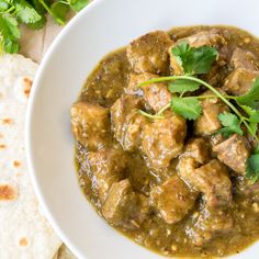 a white bowl filled with meat covered in gravy and garnished with cilantro