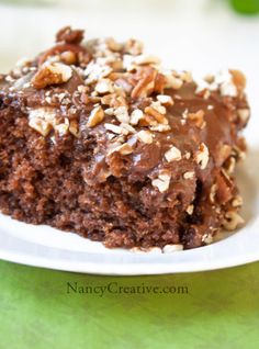 a close up of a piece of cake on a plate with chocolate frosting and nuts