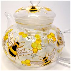 a glass tea pot with bees painted on the front and sides, sitting on a white surface