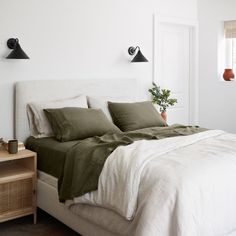 a white bed with green sheets and pillows