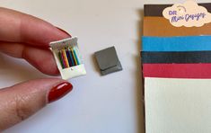 a hand holding a small box with colored pencils in it and a piece of paper next to it