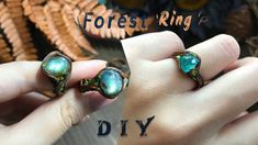 two rings with green and blue stones on them, one is being held by someone's hand