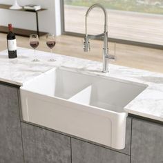 a white sink sitting under a kitchen faucet next to a wine glass and bottle