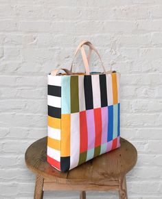 a multicolored tote bag sitting on top of a wooden stool next to a white brick wall