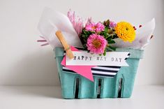 a basket filled with flowers sitting on top of a white table next to a sign that says happy may day