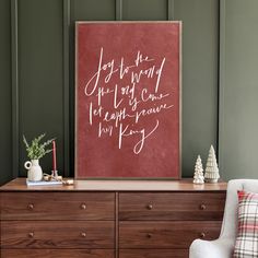 a wooden dresser topped with a red sign and christmas decorations next to a white chair