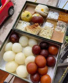 two boxes filled with different types of food on top of a table next to a red car