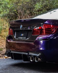 the back end of a purple bmw car parked in front of some bushes and trees