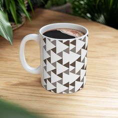 a cup of coffee sitting on top of a wooden table next to a potted plant