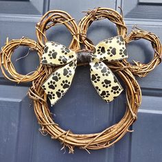 a dog paw print bow hangs on a grapevine wreath that is hanging on the front door