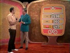 two men standing next to each other in front of a large screen with numbers on it