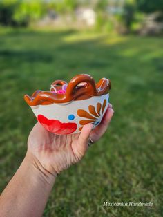 a hand holding up a bowl with food in it's mouth on the grass