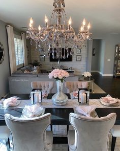 a chandelier hangs over a dining room table set for four with pink roses in the center