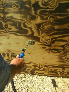 a person holding a blue and green toothbrush in their hand next to a piece of wood