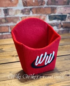 a red felt cup holder sitting on top of a wooden table next to a brick wall