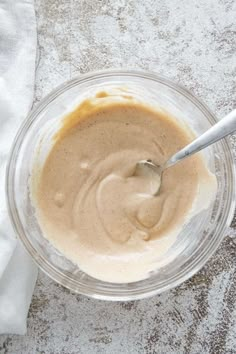 a glass bowl filled with batter on top of a white tablecloth next to a spoon