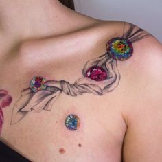 a woman's chest with three different colored jewels on her left shoulder and the upper part of her right arm