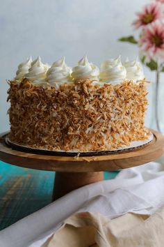 a close up of a cake on a wooden platter with flowers in the background