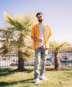 a man standing in front of a palm tree wearing sunglasses and a yellow cardigan