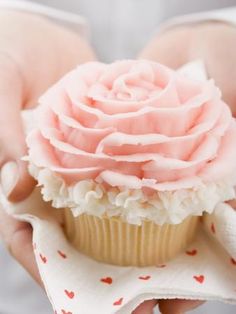 a person holding a cupcake with pink frosting