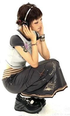 a woman sitting on top of a skateboard while talking on a cell phone and wearing headphones