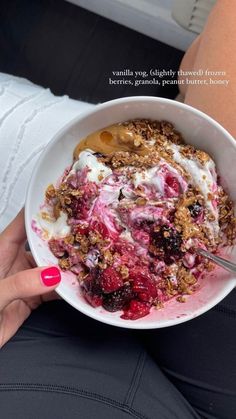 a person holding a bowl of food with yogurt and granola in it