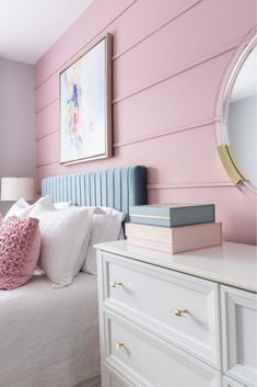 a bedroom with pink walls, white furniture and a mirror on the wall above it