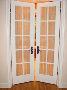 two white doors with wooden blinds on the top and bottom, in front of a doorway