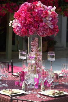 a tall vase filled with pink flowers sitting on top of a table covered in wine glasses