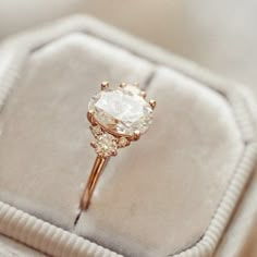 an engagement ring sitting on top of a white velvet cushion in a box with gold accents