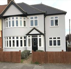 a large grey house with white windows and wooden fenced in area next to it