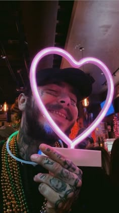 a man holding up a heart shaped neon sign in his right hand and smiling at the camera