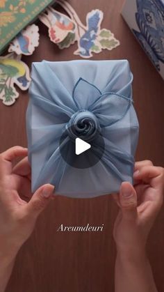 someone holding up a blue gift box with a bow on it's side and the video below