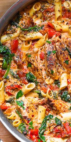 a skillet filled with pasta and vegetables on top of a wooden table