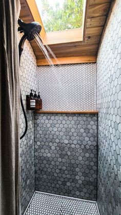 a shower head in the corner of a bathroom with tiled walls and flooring, under a skylight