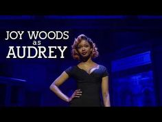 a woman standing on top of a stage in front of a blue background with the words joy woods as audrey