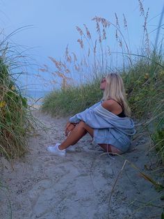 a woman is sitting on the beach by some grass