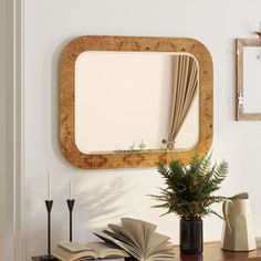 an open book on a table next to a mirror and vase with plants in it