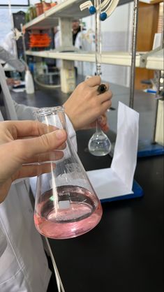 two people in white lab coats holding beakles with pink liquid