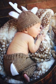 a baby wearing a knitted deer hat and diaper is sleeping in a basket