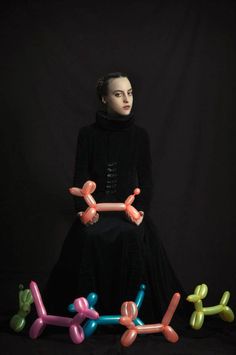 a woman standing in front of an assortment of balloon shaped objects on a black background