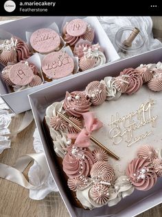 a birthday cake with pink frosting in a box and some cookies on the table