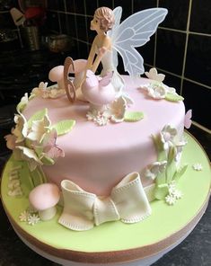 a pink cake decorated with white flowers and a fairy sitting on it's side