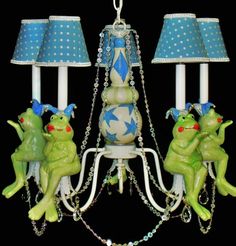 two green frogs sitting on top of a chandelier with blue and white lamps