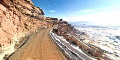 an aerial view of a dirt road next to a mountain side with snow on the ground